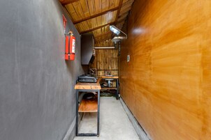 A narrow hallway with a wooden ceiling, a fire extinguisher, a table with a sink, and a bench.