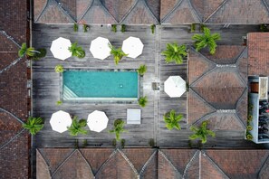 An aerial view of a rooftop pool area with a rectangular pool, surrounded by white umbrellas and palm trees, and a brick-patterned roof. - Turtle Villas Canggu (Tibubeneng)