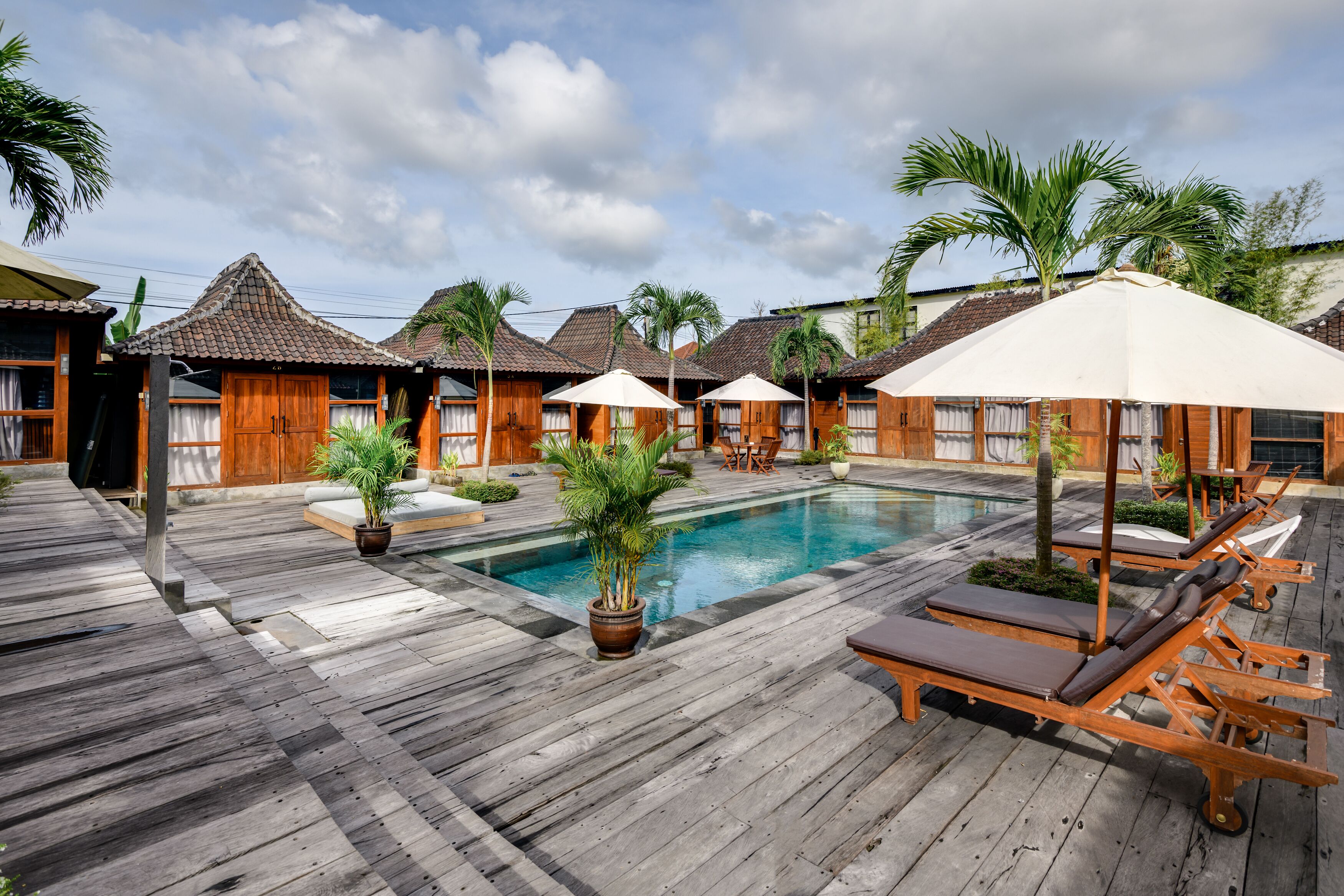 A wooden deck with a pool, lounge chairs, and umbrellas.
