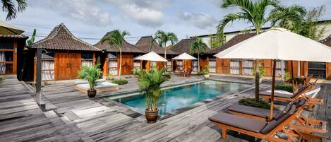 A wooden deck with a pool, lounge chairs, and umbrellas.