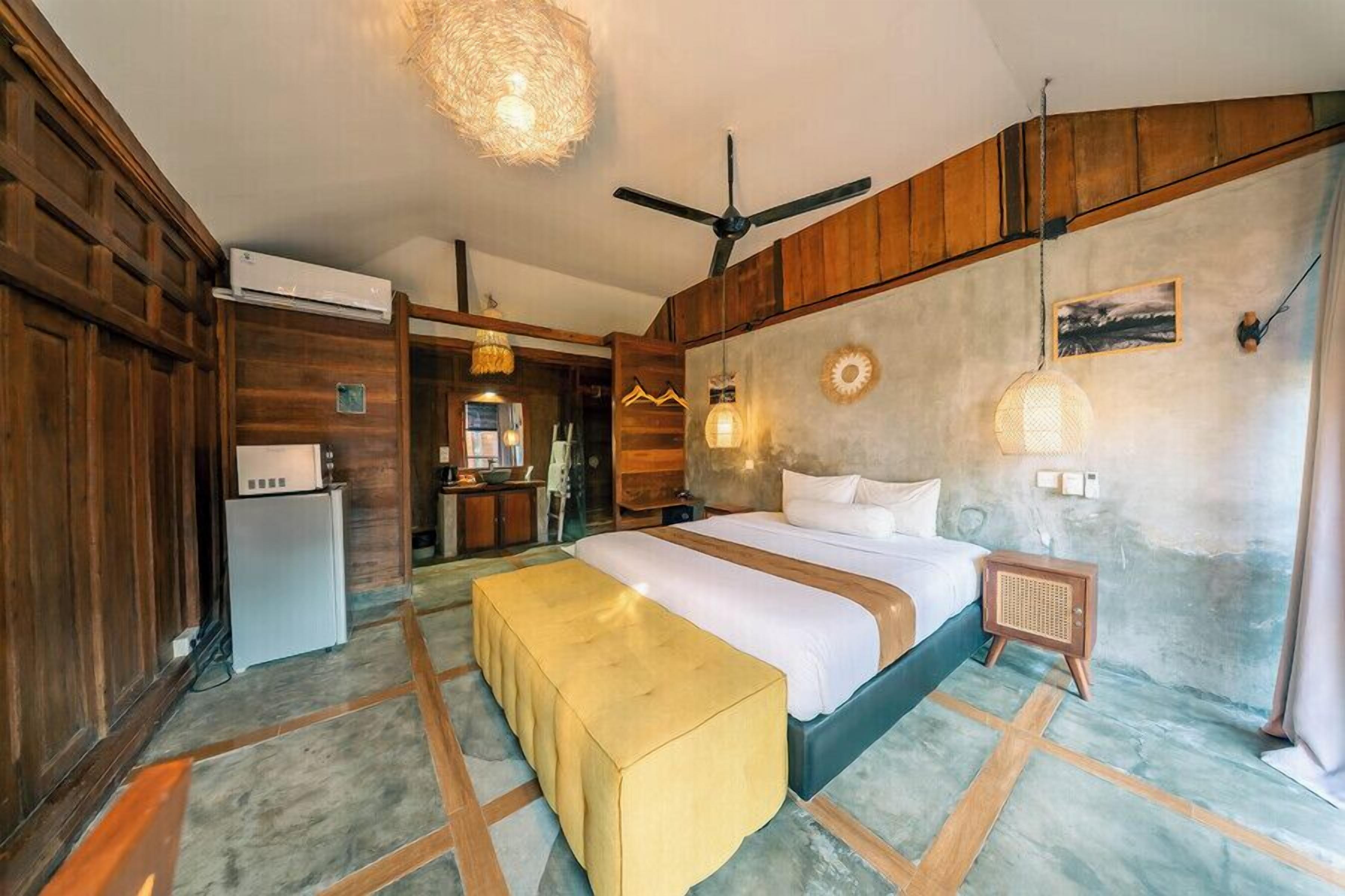 Una habitación con cama, una banca, un ventilador de techo y una lámpara fijada a la pared.