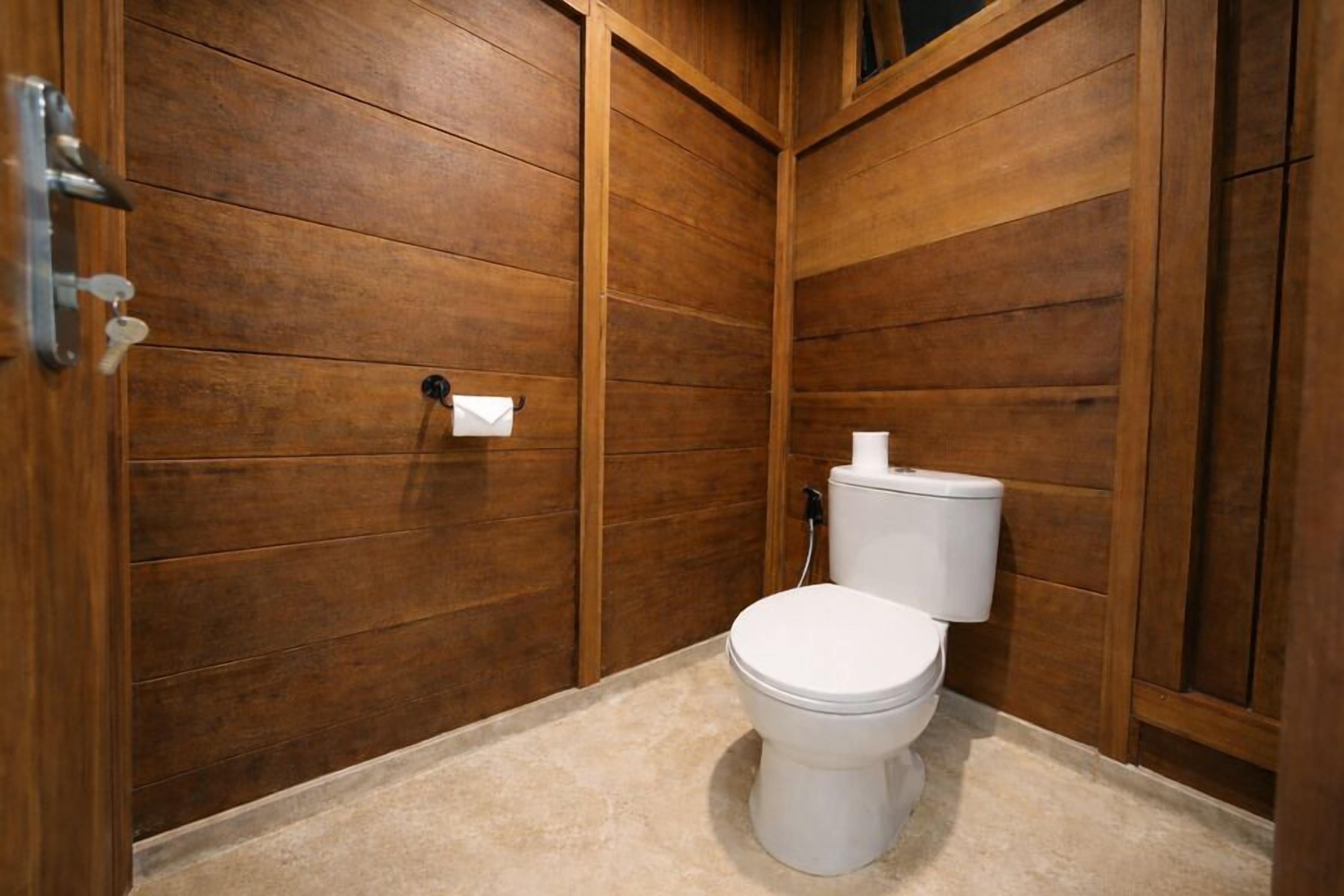 A wooden-paneled bathroom with a toilet, a towel dispenser, and a paper towel holder.
