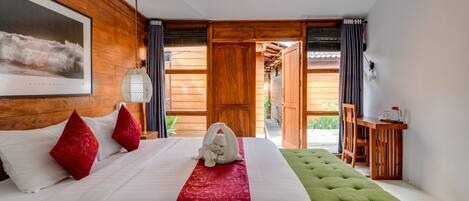 A hotel room with a large bed, a green ottoman, a wooden desk, and a view of the outdoors.