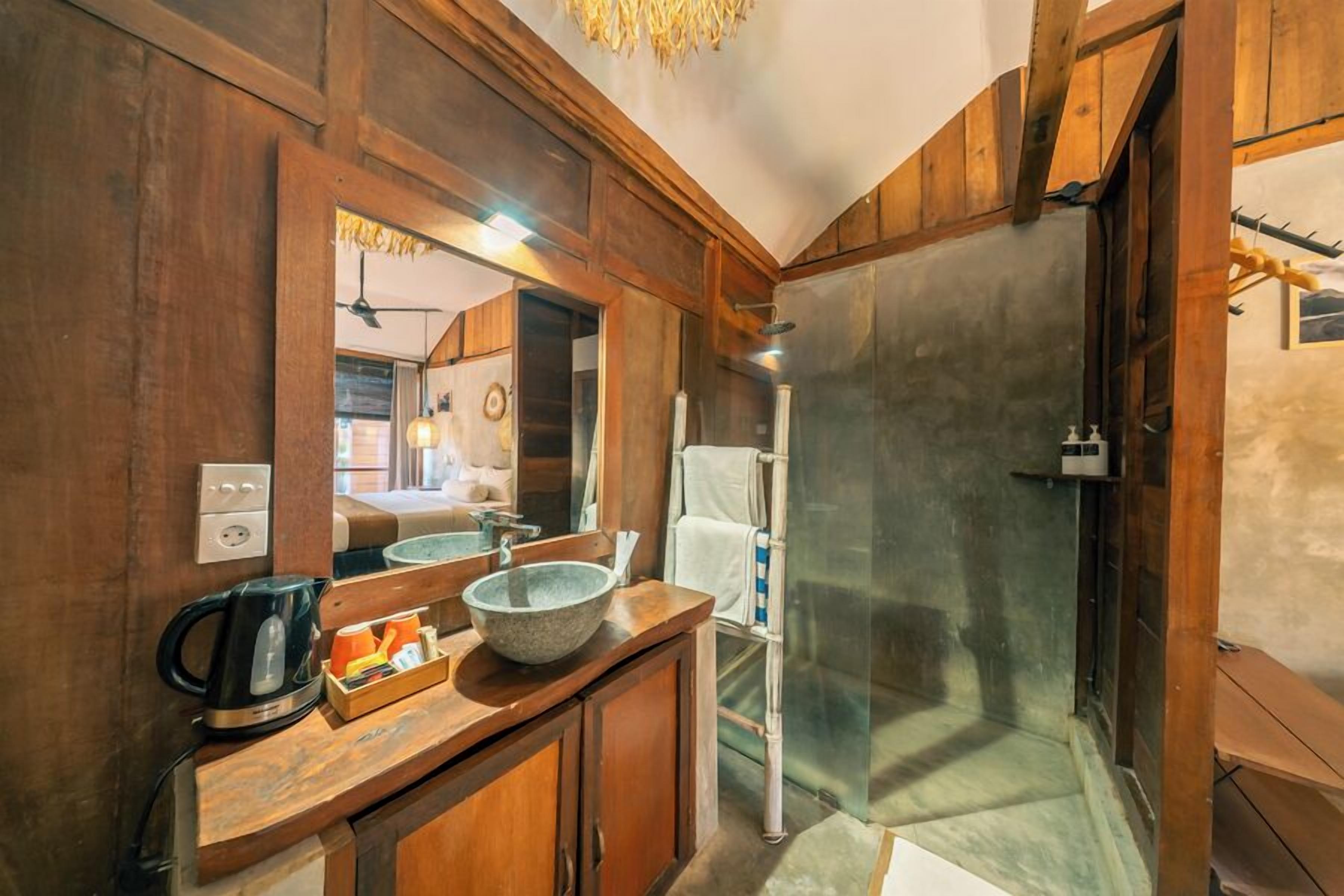 Un baño con muebles de madera, un espejo grande, una cabina de ducha de vidrio y una cafetera sobre la encimera.