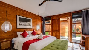 Een slaapkamer met houten lambrisering, een groot bed, een groene poef, een hanglamp en een raam met gordijnen.