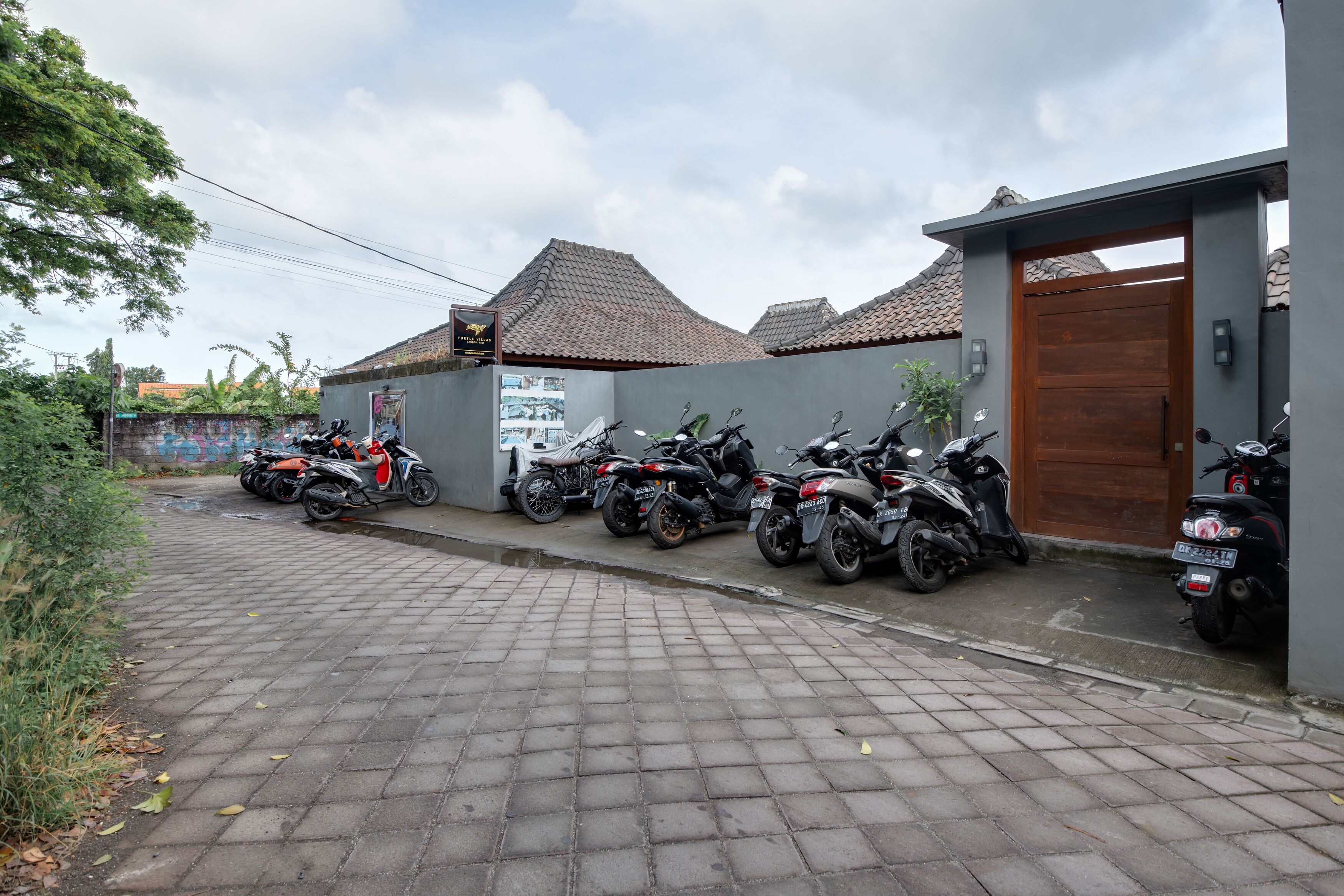 A row of motorcycles parked along a paved street in front of a building with a tiled roof and a wooden door.