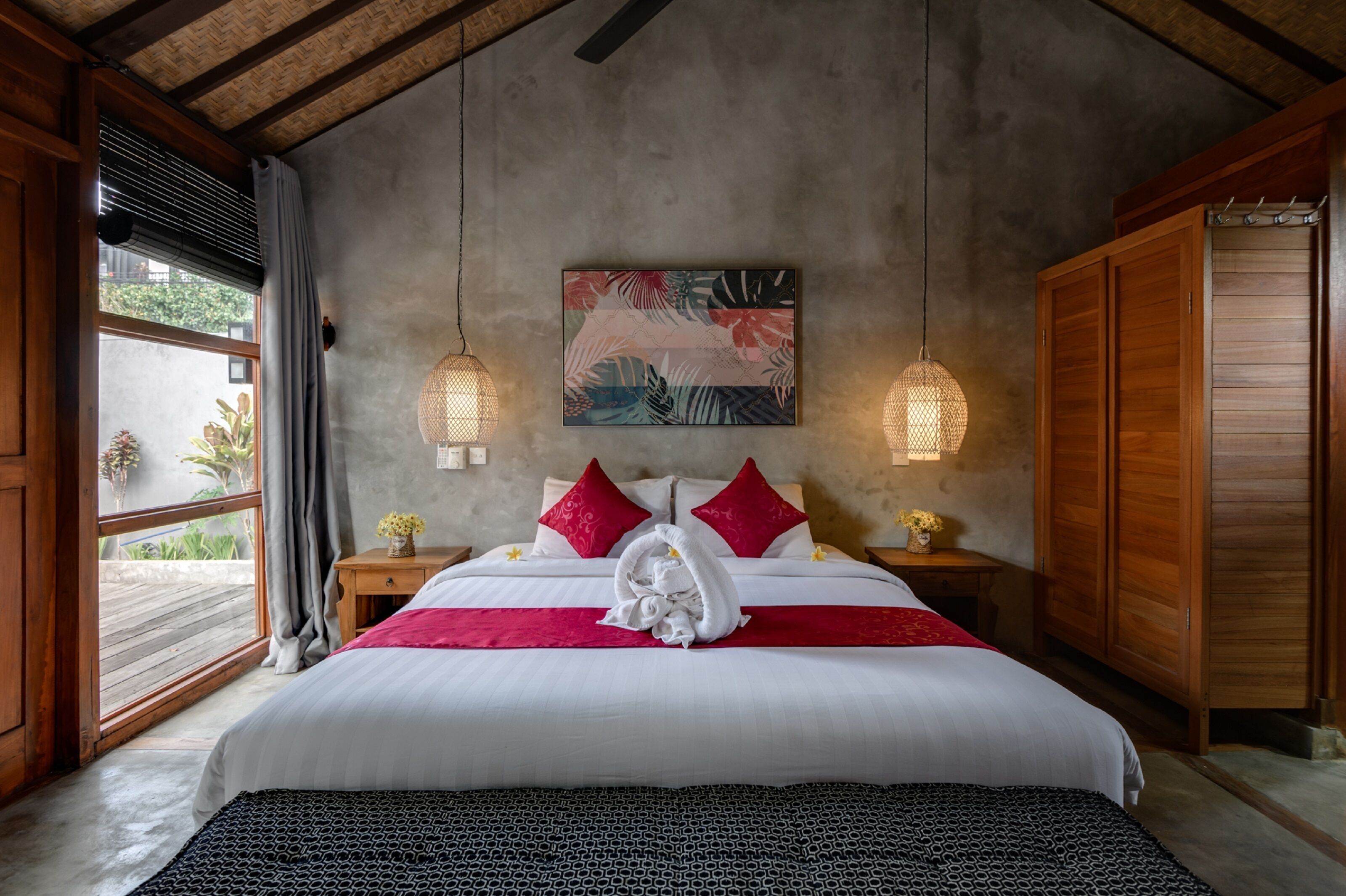 A bedroom with a large bed, a wooden wardrobe, and a concrete wall with a floral painting.