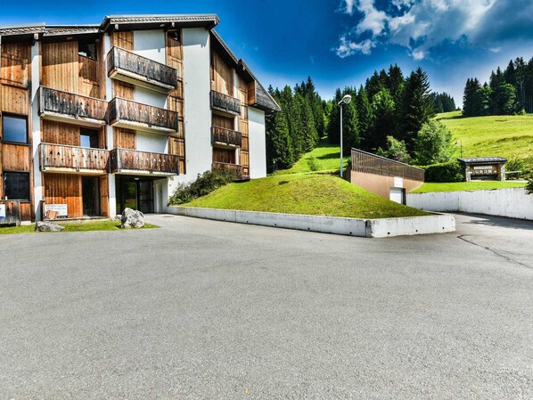 A multi-story building with wooden balconies, a grassy hill, and a clear sky. - Paméo 1 - Cozy 6-Person Duplex Near Ski Slopes in La Turche, Les Gets (Les Gets)