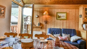A cozy room with a wooden ceiling, a dining table set with plates and glasses, a blue sofa with cushions, and a wall-mounted clock. - Paméo 1 - Cozy 6-Person Duplex Near Ski Slopes in La Turche, Les Gets (Les Gets)
