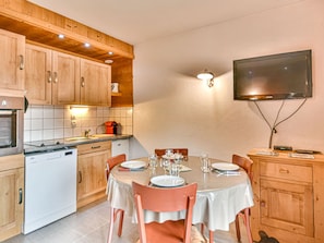 Cozinha com armários de madeira, uma mesa de jantar posta para quatro pessoas e uma TV de tela plana presa à parede.
