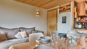 A cozy living room with a sofa, a dining table set with bowls and glasses, and a wooden ceiling. - Cozy 1BR + Alcove, Balcony, Near Slopes and Town, Sleeps 6 (Les Gets)