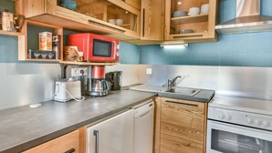 A compact kitchen with wooden cabinets, a red microwave, a coffee maker, a toaster, and a sink. - Cozy 1BR + Alcove, Balcony, Near Slopes and Town, Sleeps 6 (Les Gets)