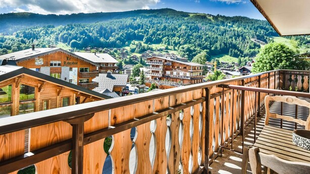 A wooden balcony with a view of a village and mountains. - Cozy 1BR + Alcove, Balcony, Near Slopes and Town, Sleeps 6 (Les Gets)