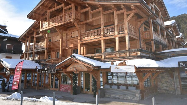 Een houten chalet met meerdere balkons en een bordje met 'Agence Olivier'.