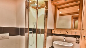 Een moderne badkamer met een douchecabine van glas, een witte wastafel en houten kastjes.