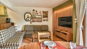 A cozy living room with a sofa set, a wooden coffee table, and a TV mounted on a wooden panel wall. - Duplex T3 in Les Gets - 5 pers, panoramic view, balcony, parking, WiFi (Les Gets)