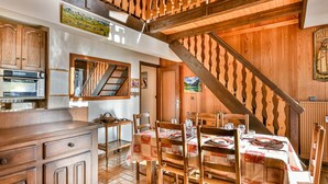 Un interior rústico con vigas de madera, un comedor listo para cuatro personas y una cocina con electrodomésticos modernos.