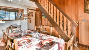 Un comedor con una escalera de madera, una mesa dispuesta para cuatro personas y vistas al exterior a través de una ventana.