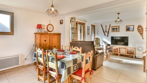 A dining area with a wooden table and chairs, a television, and a cabinet. - New Ski-in/Ski-out 2BR in Les Gets - Ideal Location with Balconies & WiFi (Les Gets)