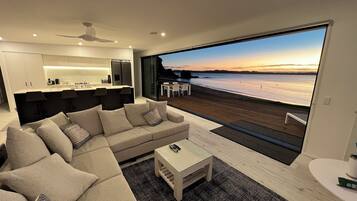 Un salon moderne avec un grand canapé, une table basse et une vue sur une plage au coucher du soleil.