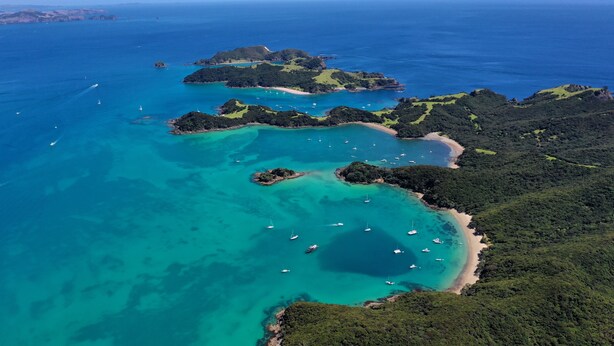 Vue aérienne d’une zone côtière avec des eaux turquoise limpides, plusieurs petites îles et des bateaux ancrés près du rivage.