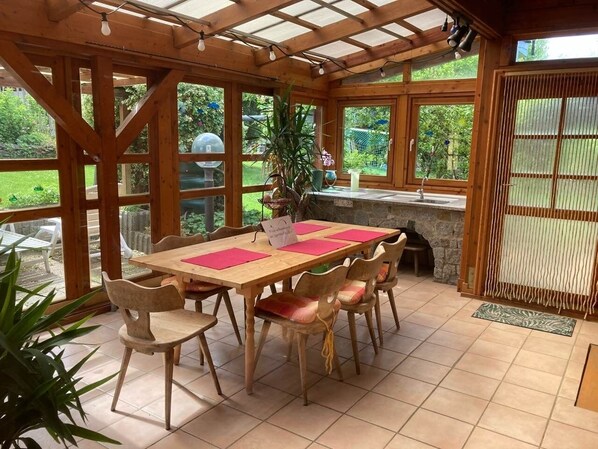 Un coin repas en bois, avec une table et des chaises, de grandes fenêtres et une vue sur le jardin.