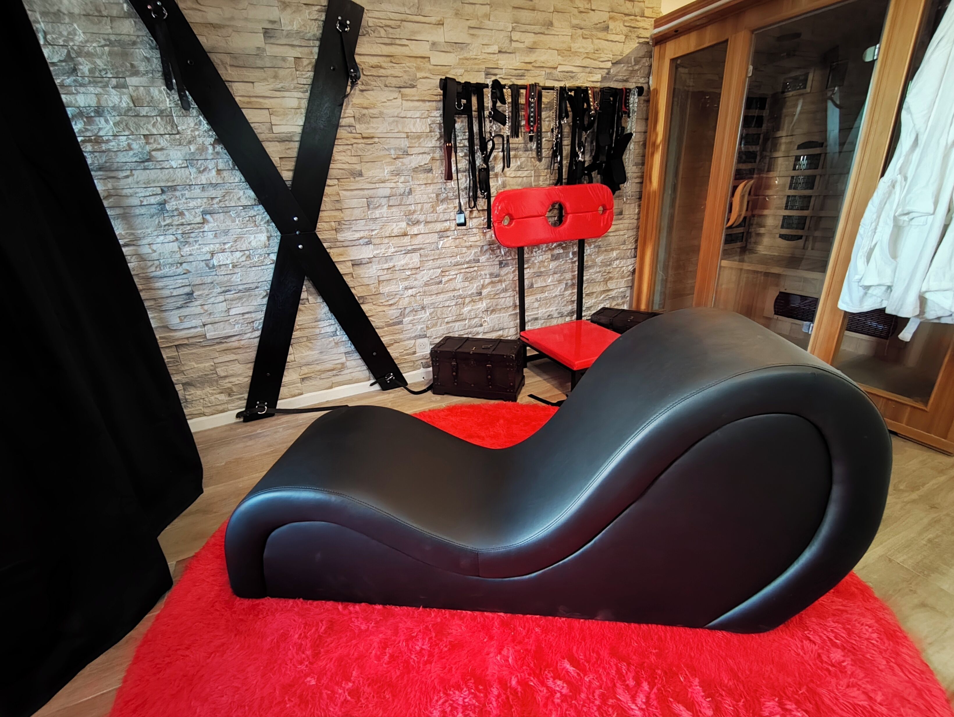 A room with a black massage chair, a red rug, a stone wall, and a wooden cabinet.