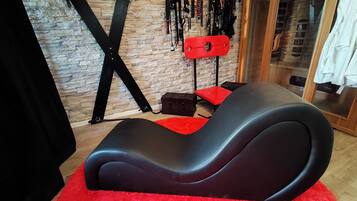 A room with a black massage chair, a red rug, a stone wall, and a wooden cabinet.