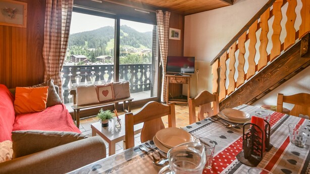 Une pièce chaleureuse avec un balcon, des meubles en bois et une table à manger dressée pour deux personnes.