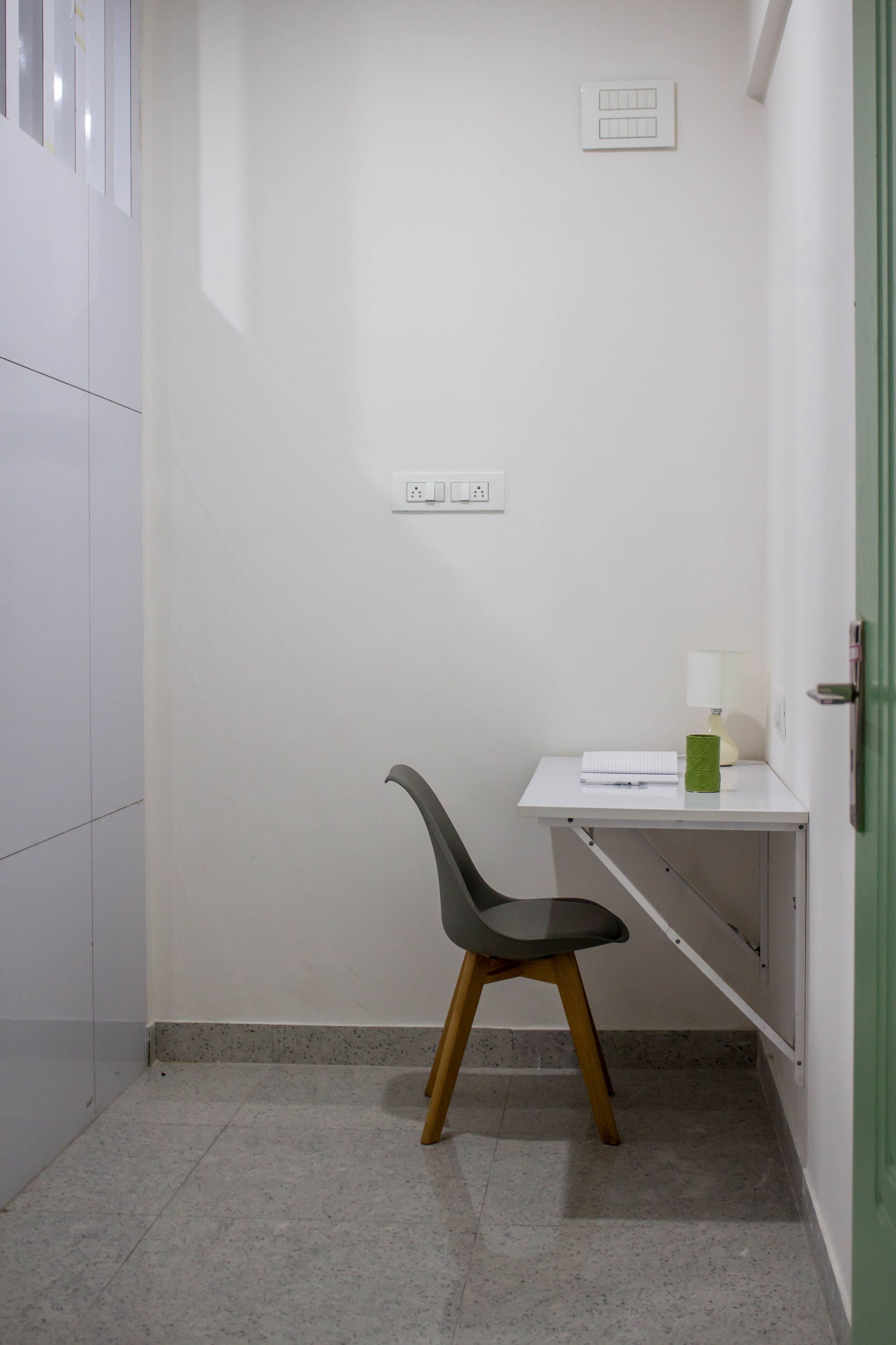 A small, clean room with a single chair, a white desk, and a green door.