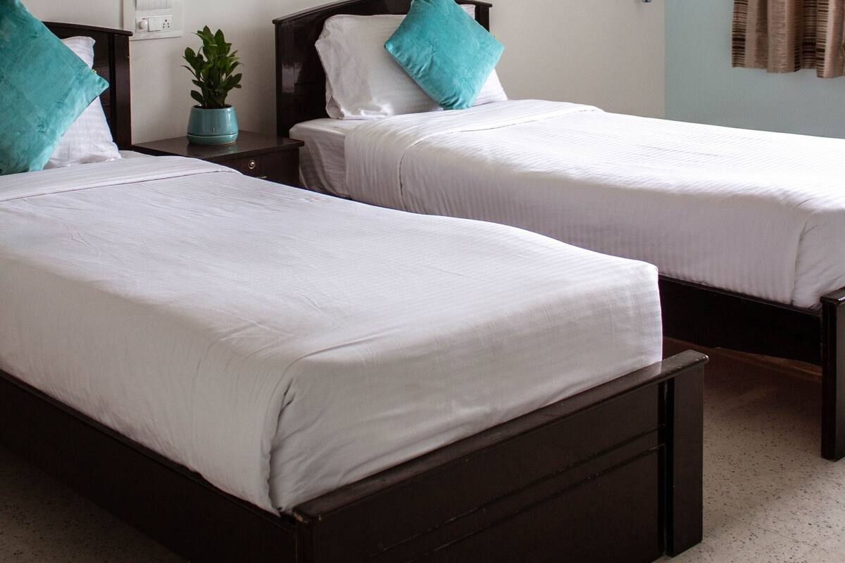 Habitación de hotel con dos camas individuales, un cuadro en la pared, aire acondicionado y una ventana con cortinas.