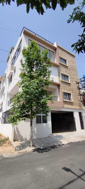 Um edifício de vários andares com varandas, uma árvore na frente e uma porta de garagem.