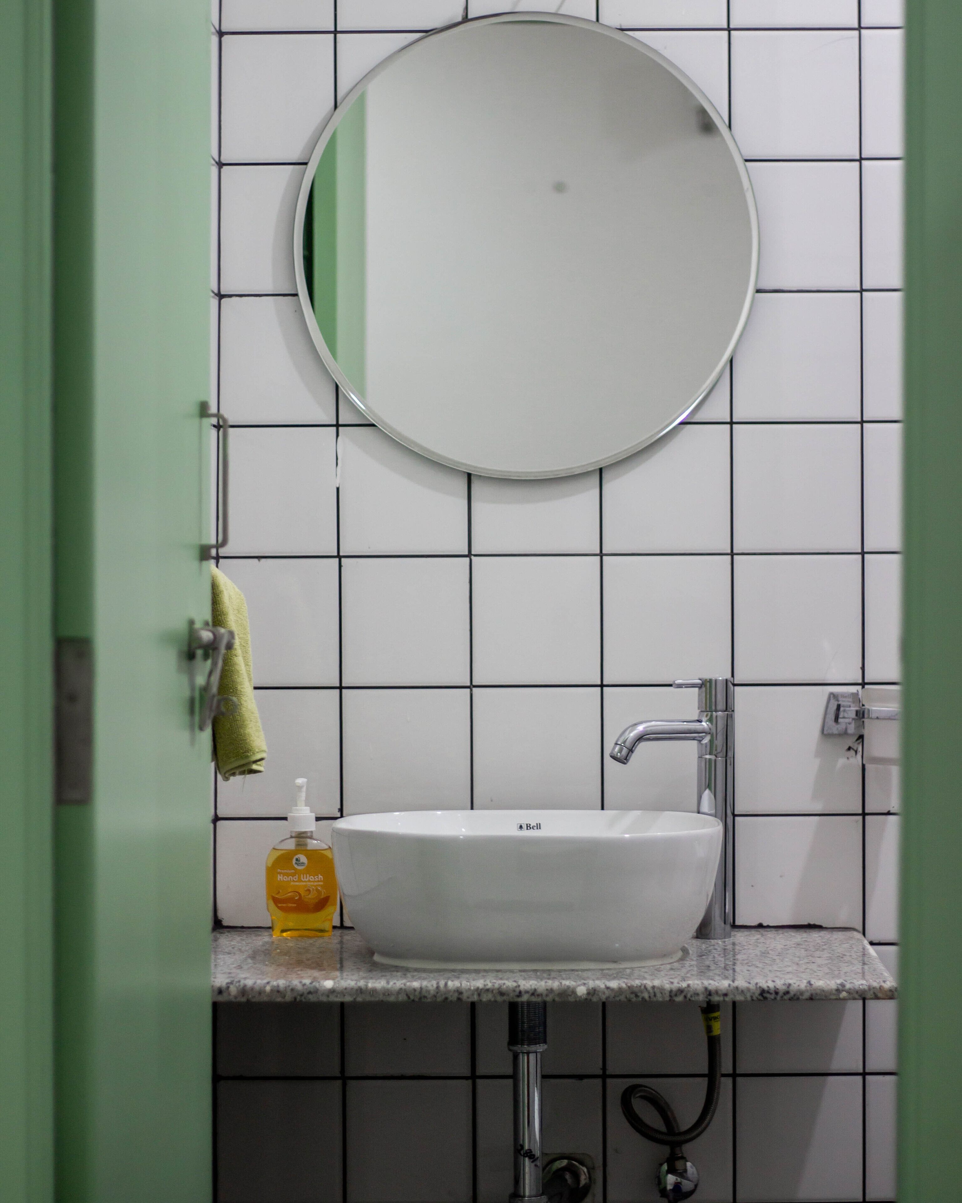 A bathroom with a white sink, a round mirror, and a green towel hanging on a rack.