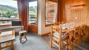 Ein Zimmer mit Holzwänden, einem Esstisch für vier Personen, einem kleinen Hocker und einem Fenster mit Blick auf eine gebirgige Landschaft.