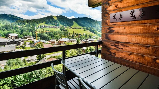 Ein Holzbalkon mit Tisch und Stühlen mit Blick auf eine Berglandschaft mit Häusern und einer Straße.