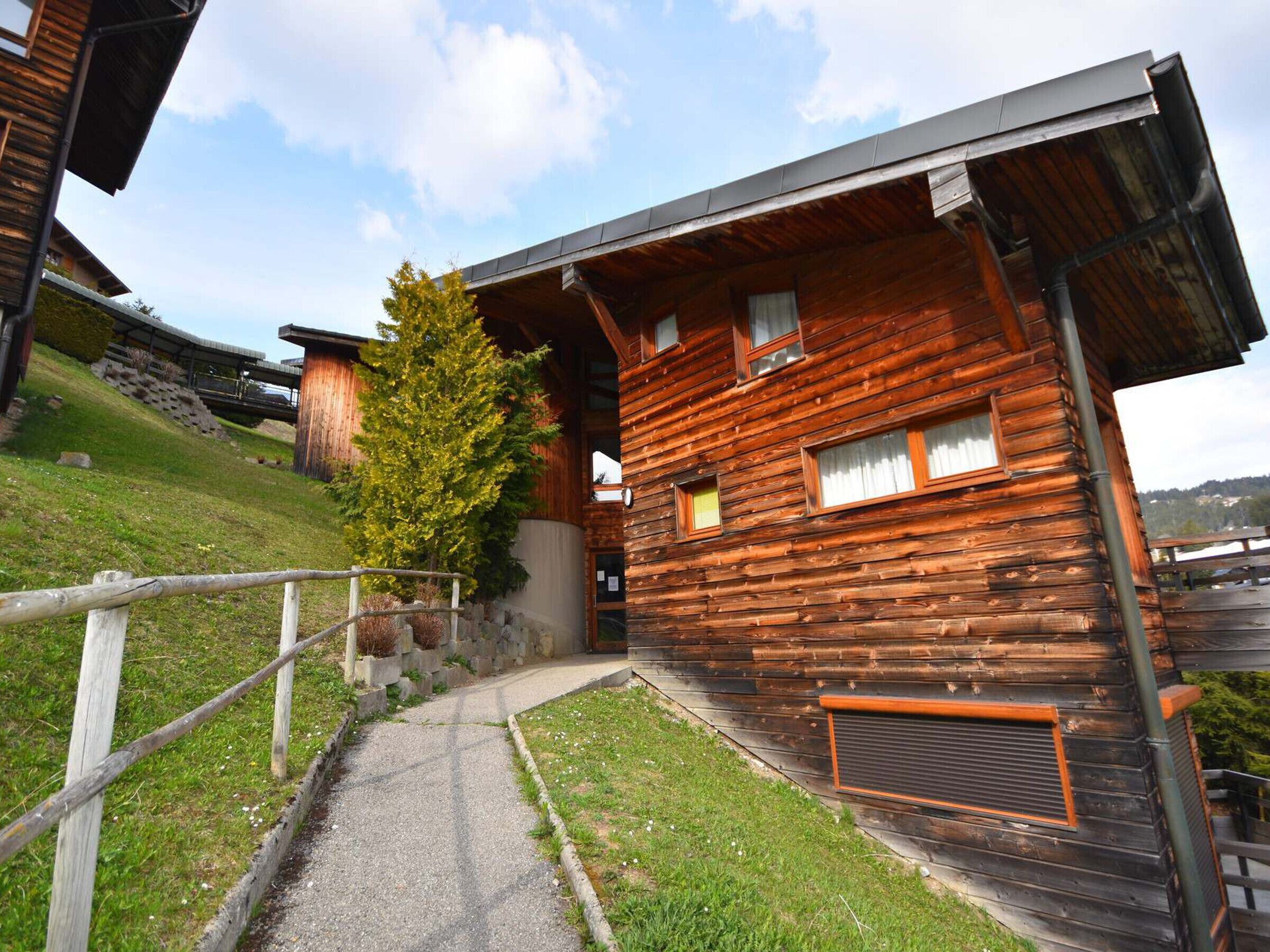 Eine Holzhütte mit geneigtem Dach, einem sichtbaren Schornstein und einem Weg zum Eingang.