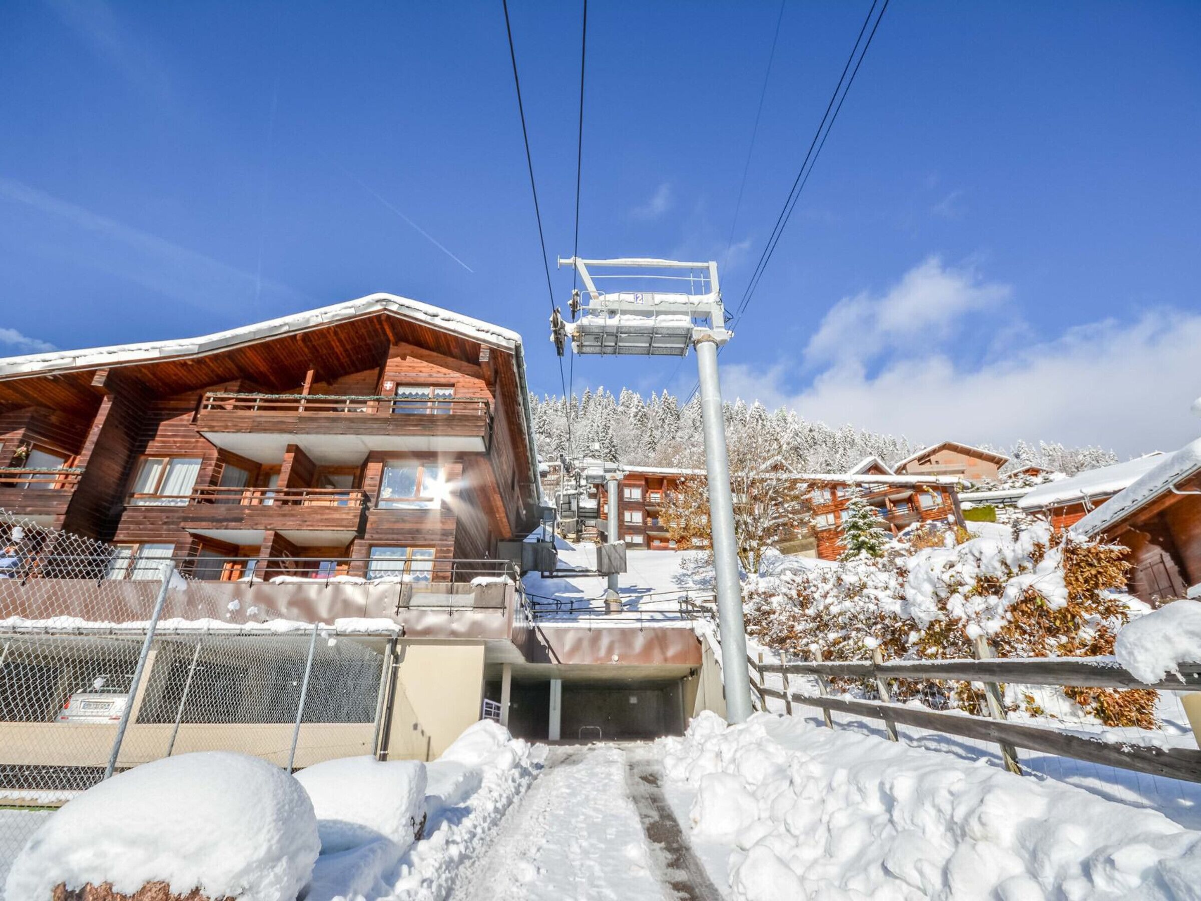 Een houten chalet met een balkon, een skilift en een besneeuwde berg op de achtergrond.