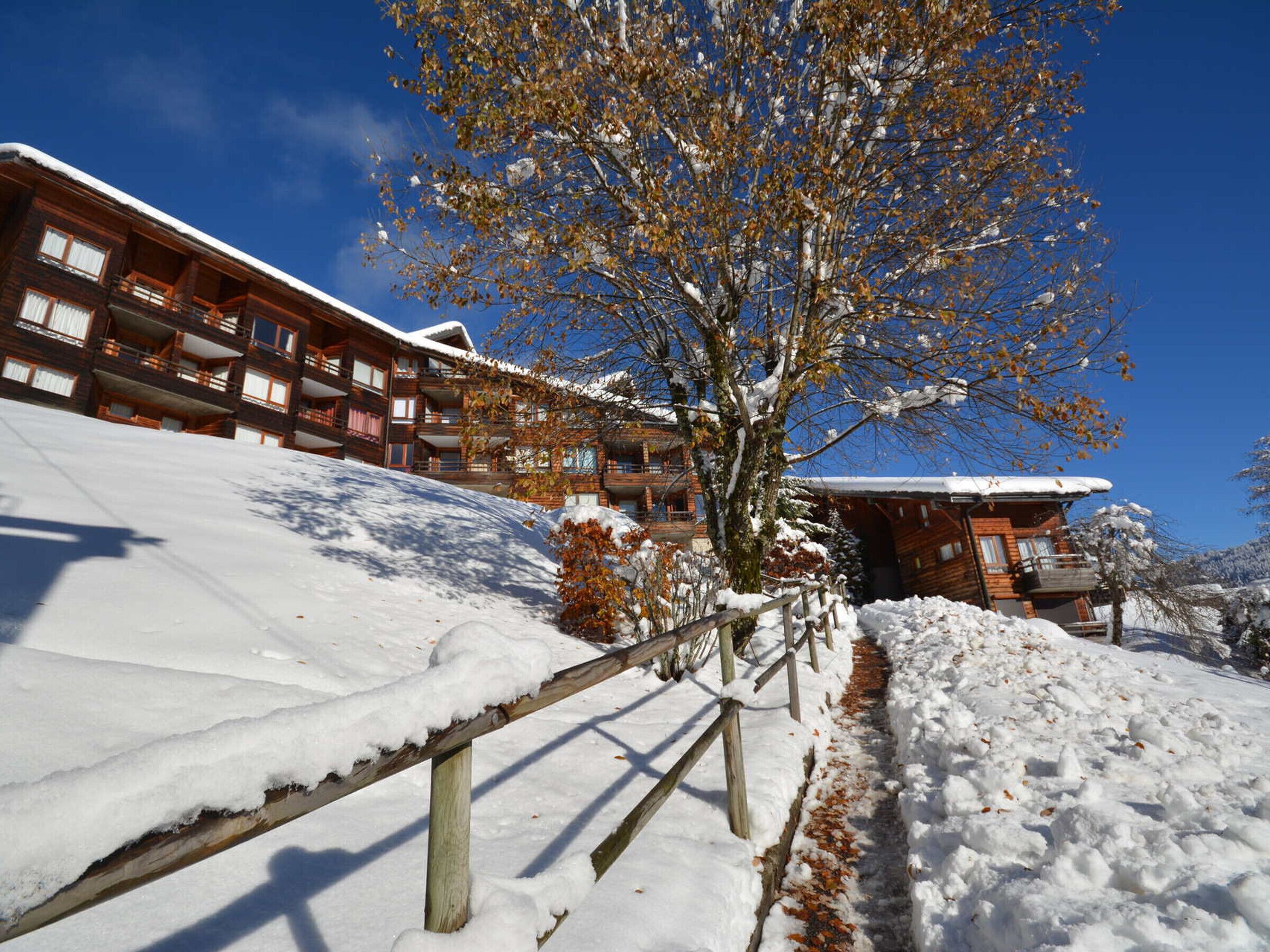 A snow-covered building with multiple balconies and a wooden fence.