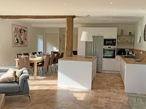 Eine moderne Küche mit weißen Schränken, einer zentralen Kochinsel und einem Essbereich mit Holztisch und Stühlen.