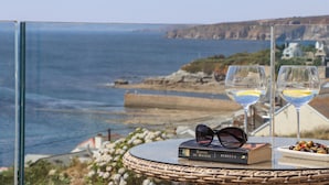 Una mesa con un libro, unas gafas de sol y un plato de aceitunas, con vistas a la costa.