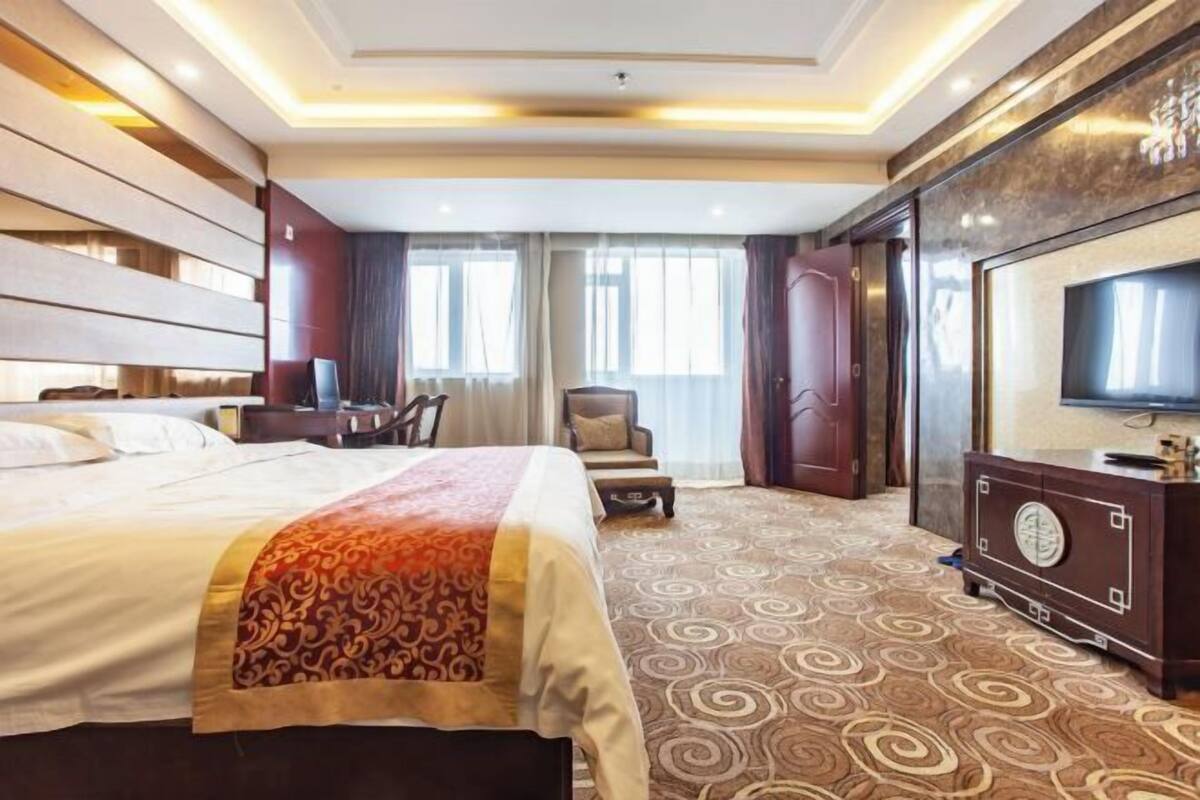 A hotel room with a large bed, a TV, a desk, and a chair.