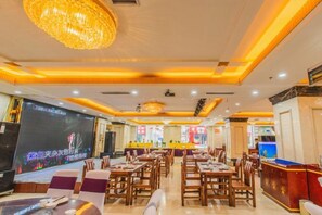 A restaurant with multiple dining tables and chairs, a large screen for presentations, and a bar area.