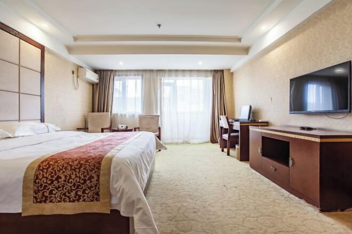 Een hotelkamer met een groot bed, een bureau met stoel, een flatscreen televisie en een groot raam met gordijnen.