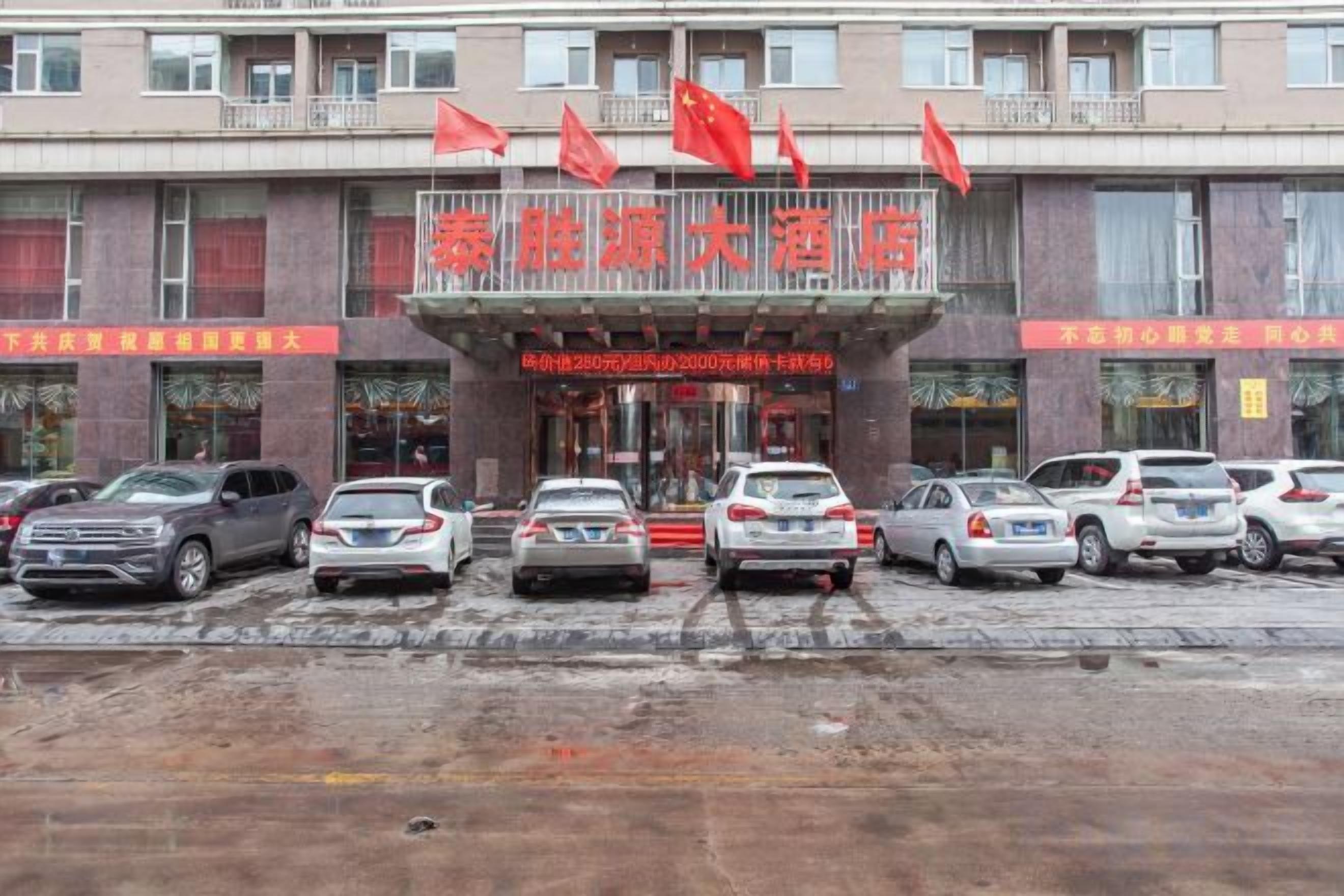 A hotel entrance with multiple cars parked in front, a red sign with Chinese characters, and several flags above.