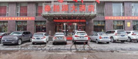 A hotel entrance with multiple cars parked in front, a red sign with Chinese characters, and several flags above.