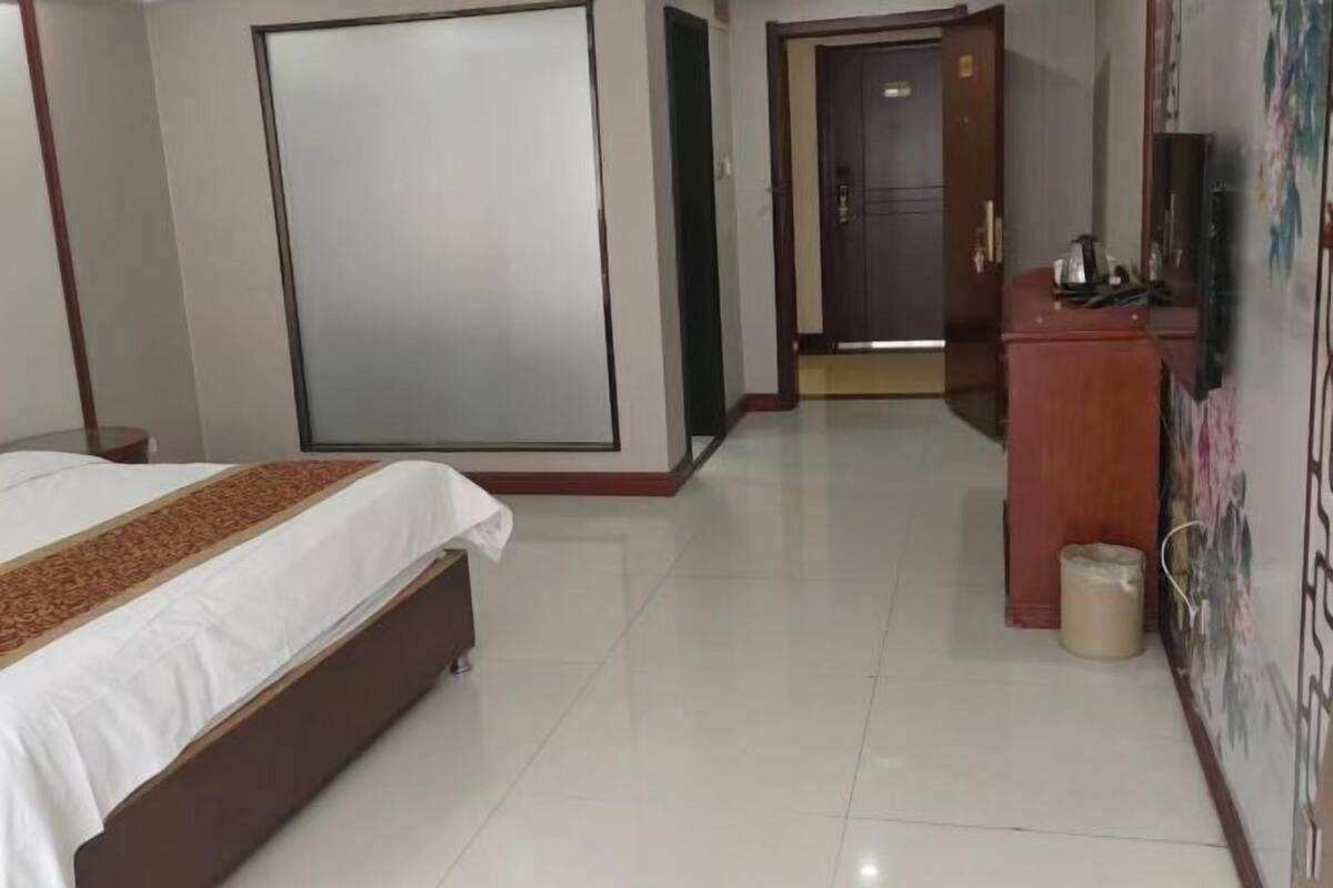 A hotel room with a bed, a wardrobe, a desk with a television, and a wall with a floral pattern.