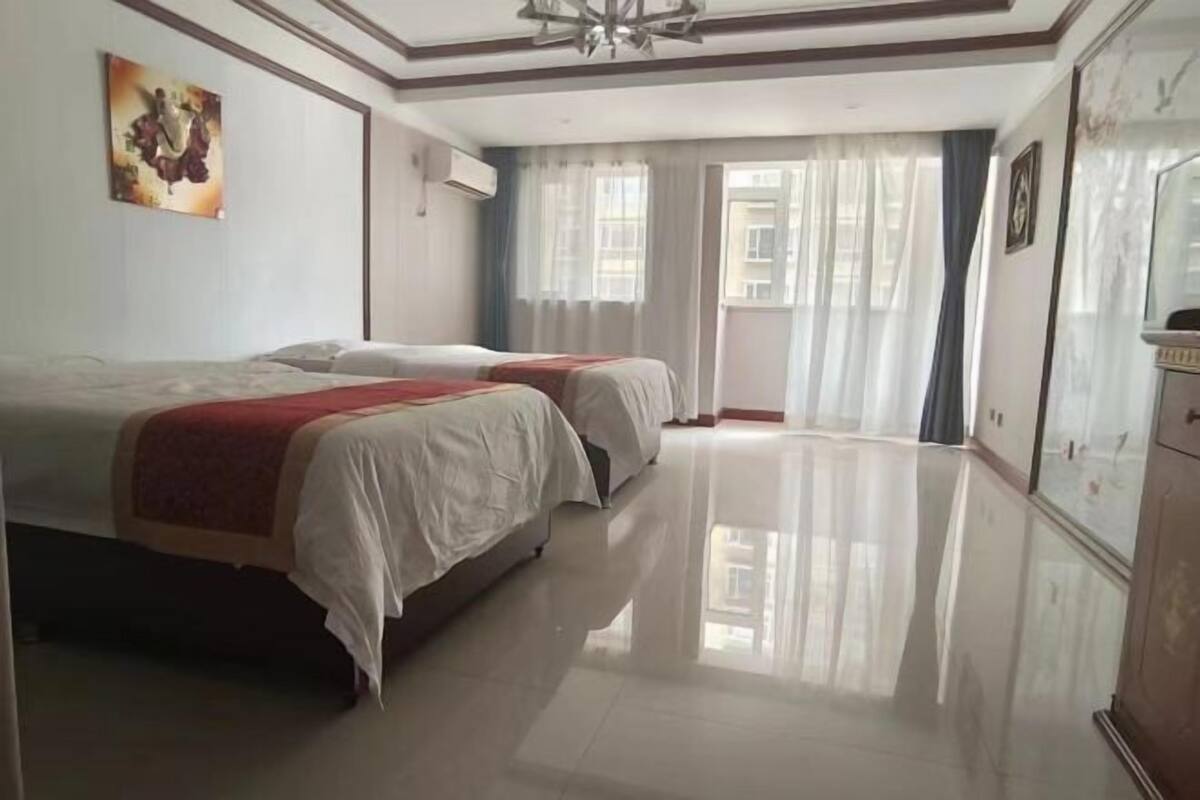 A hotel room with two beds, a large mirror, and a view of the outside through a window with curtains.
