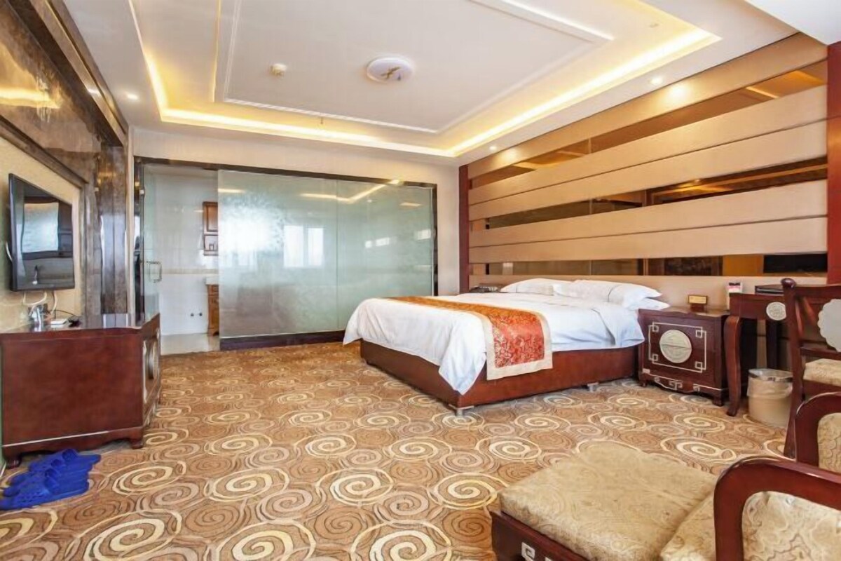 Een hotelkamer met een groot bed, een flatscreen televisie, een houten dressoir en een kamerbreed tapijt met dessin.