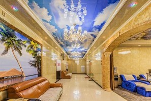 Een hotellobby met een strandmuur, lederen zitplaatsen, een kroonluchter en een blauwe bank.