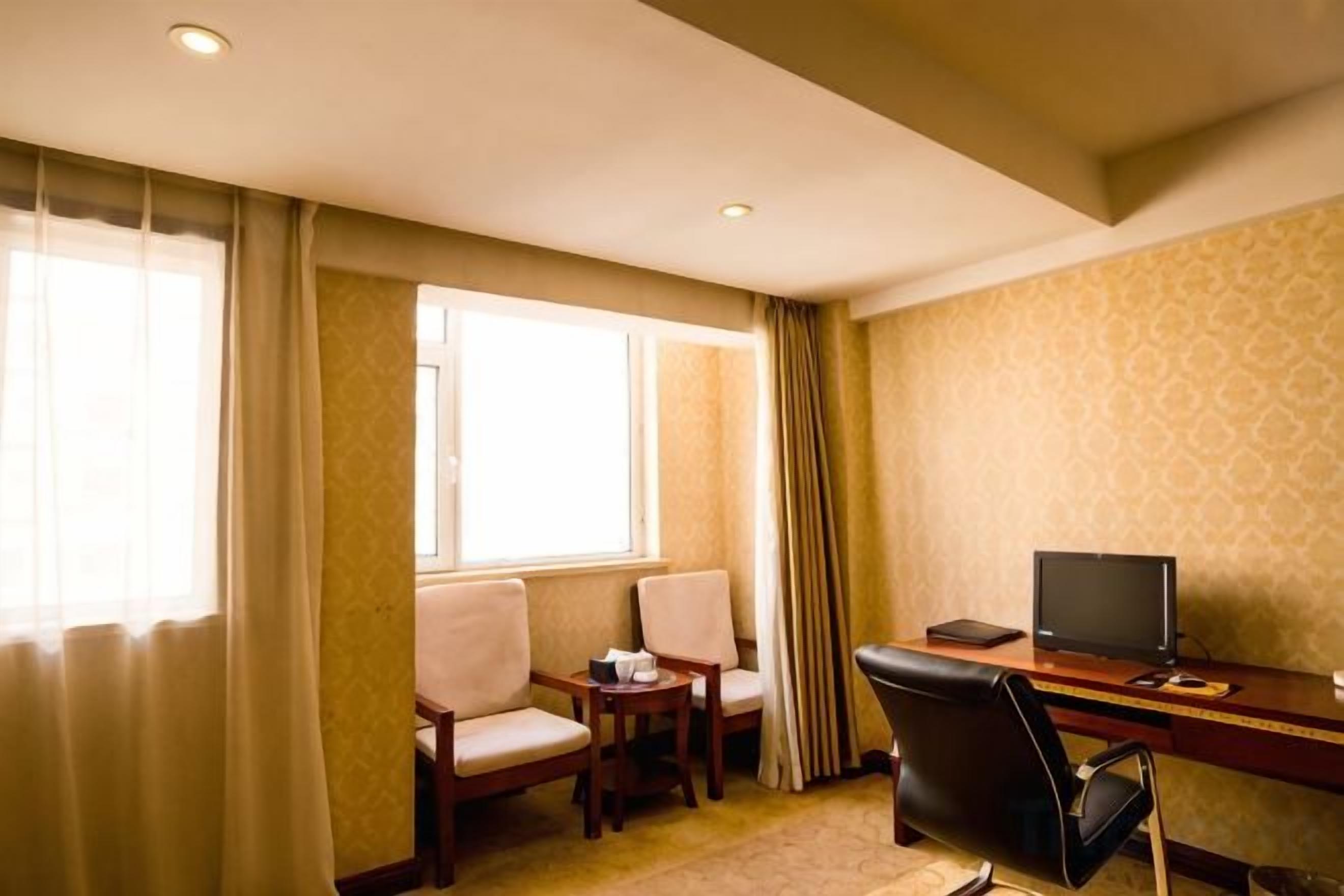 A hotel room with a desk, two chairs, a television, and a window with curtains.